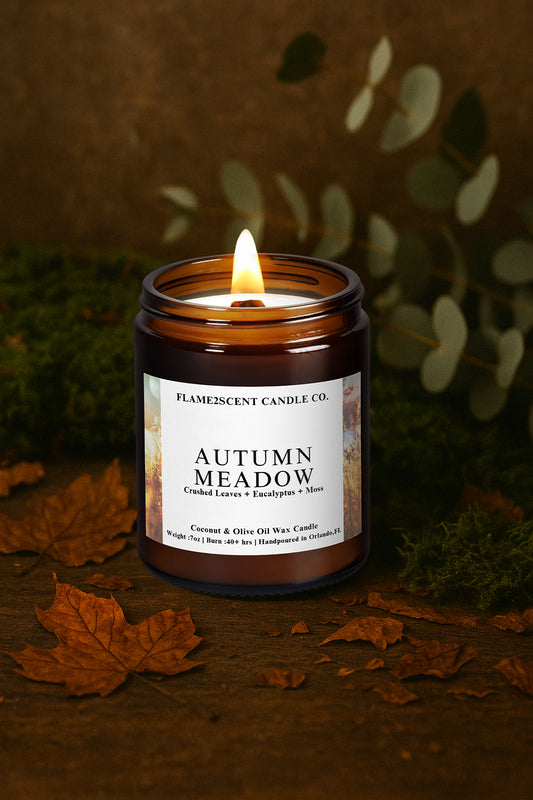 Candle labeled 'Autumn Meadow' from Flamescent Candle Co. on a dark background with leaves.